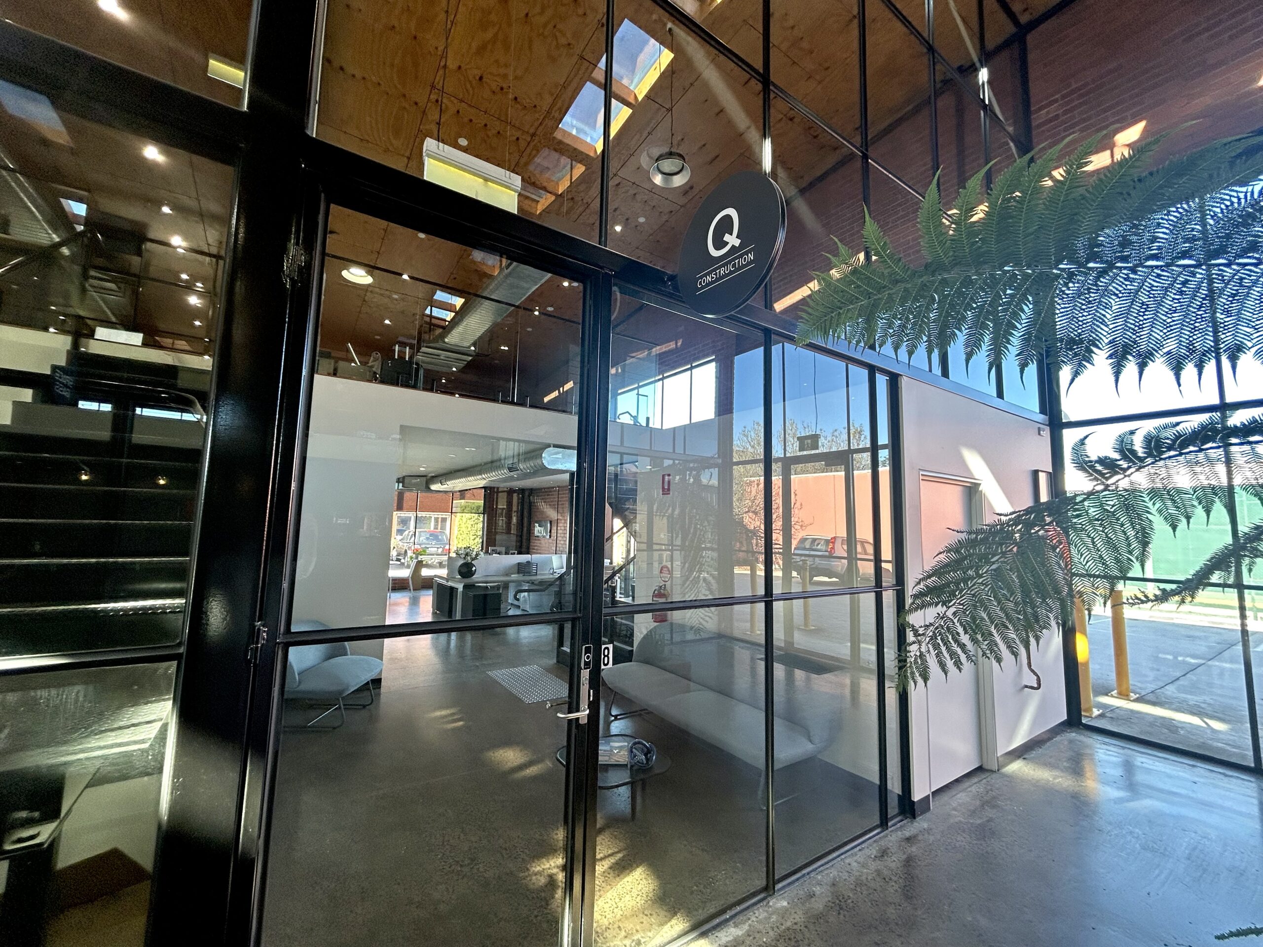 Internal view of a large office space, windows and doors cover the front of the tenancy, through the windows is a black staircase and over top is a timber roof, Hamilton property Group