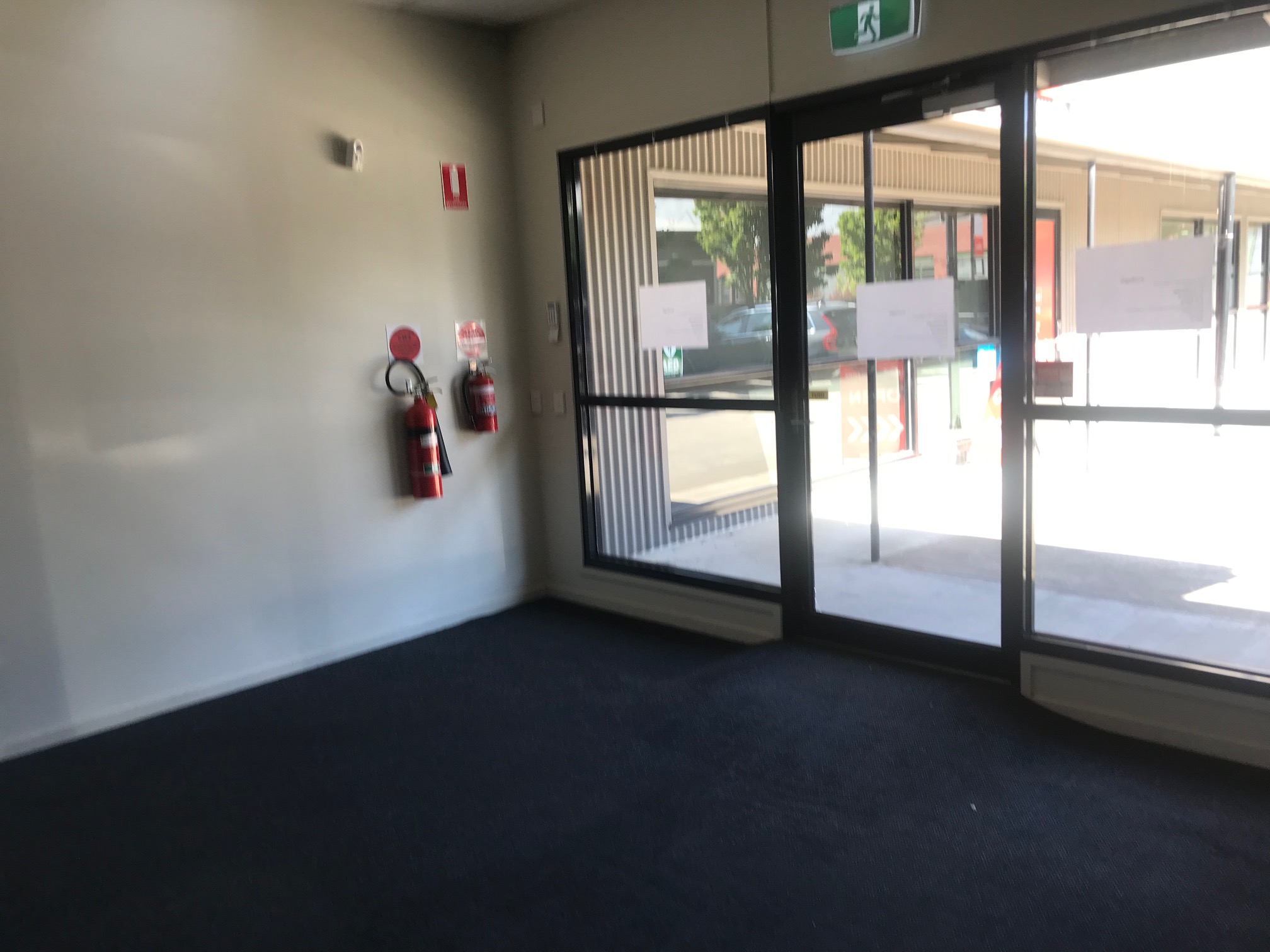 Small room with dark carpet, a door and two windows either side, white walls all around and a fire extinguisher on the wall, Hamilton Group Geelong