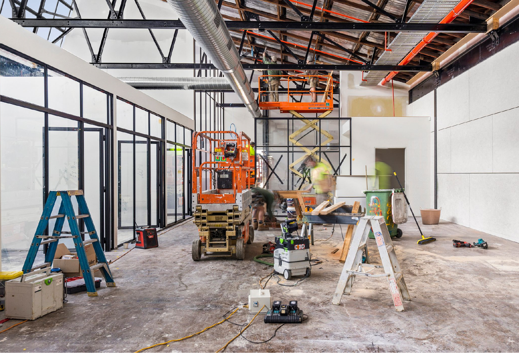 Internal demolition and reconstruction of office space, tbar windows and doors run along the left side of the building, scissor lifts are being used to reach the roof trusses - Demolition completed by Bay Side Demo