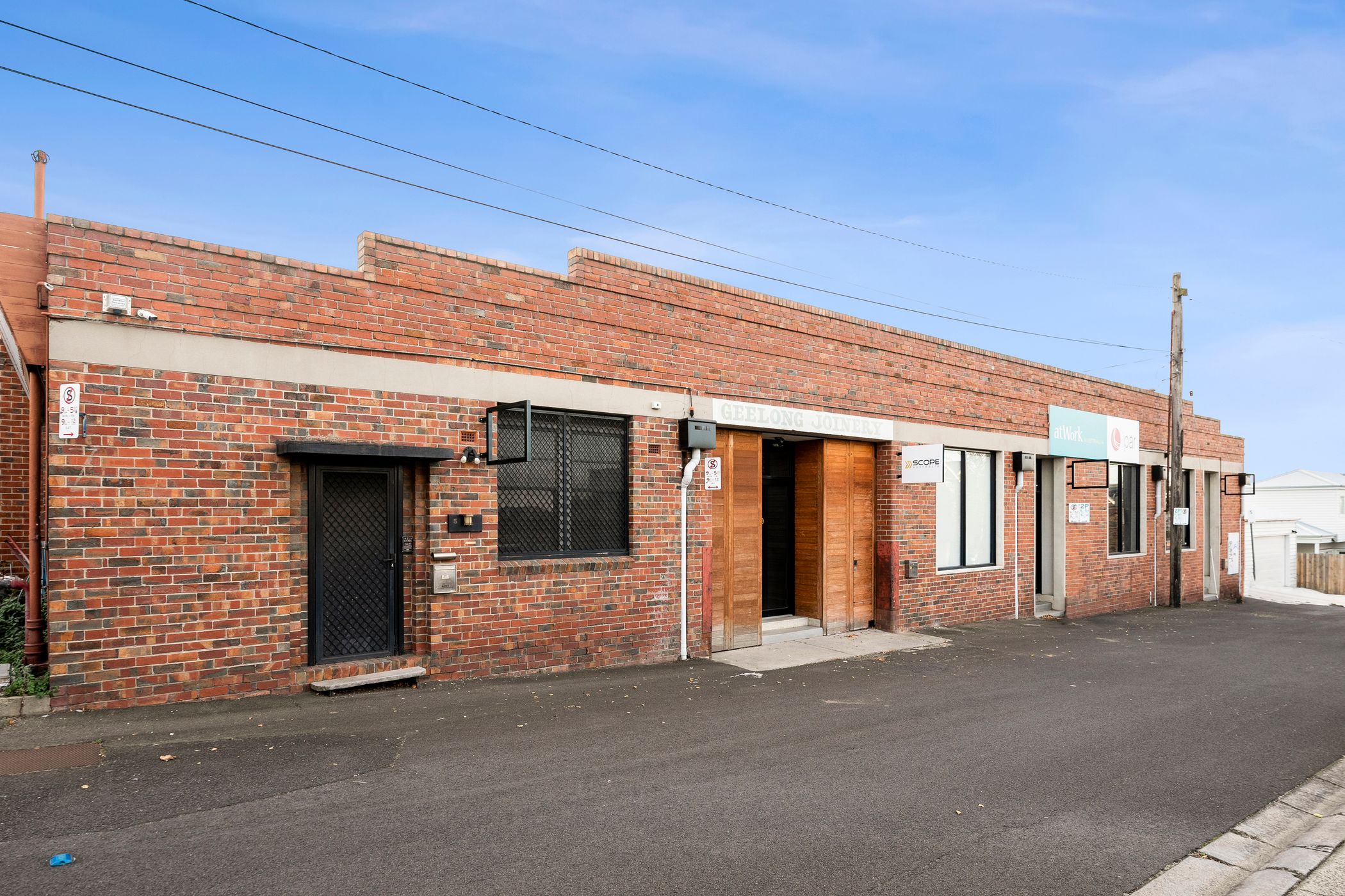 Clear blue sky above, old facade with many different colour bricks throughout, a large doorway in the middle features old timber and a sign above says "Geelong Joinery" Building leased by Hamilton Property Geelong
