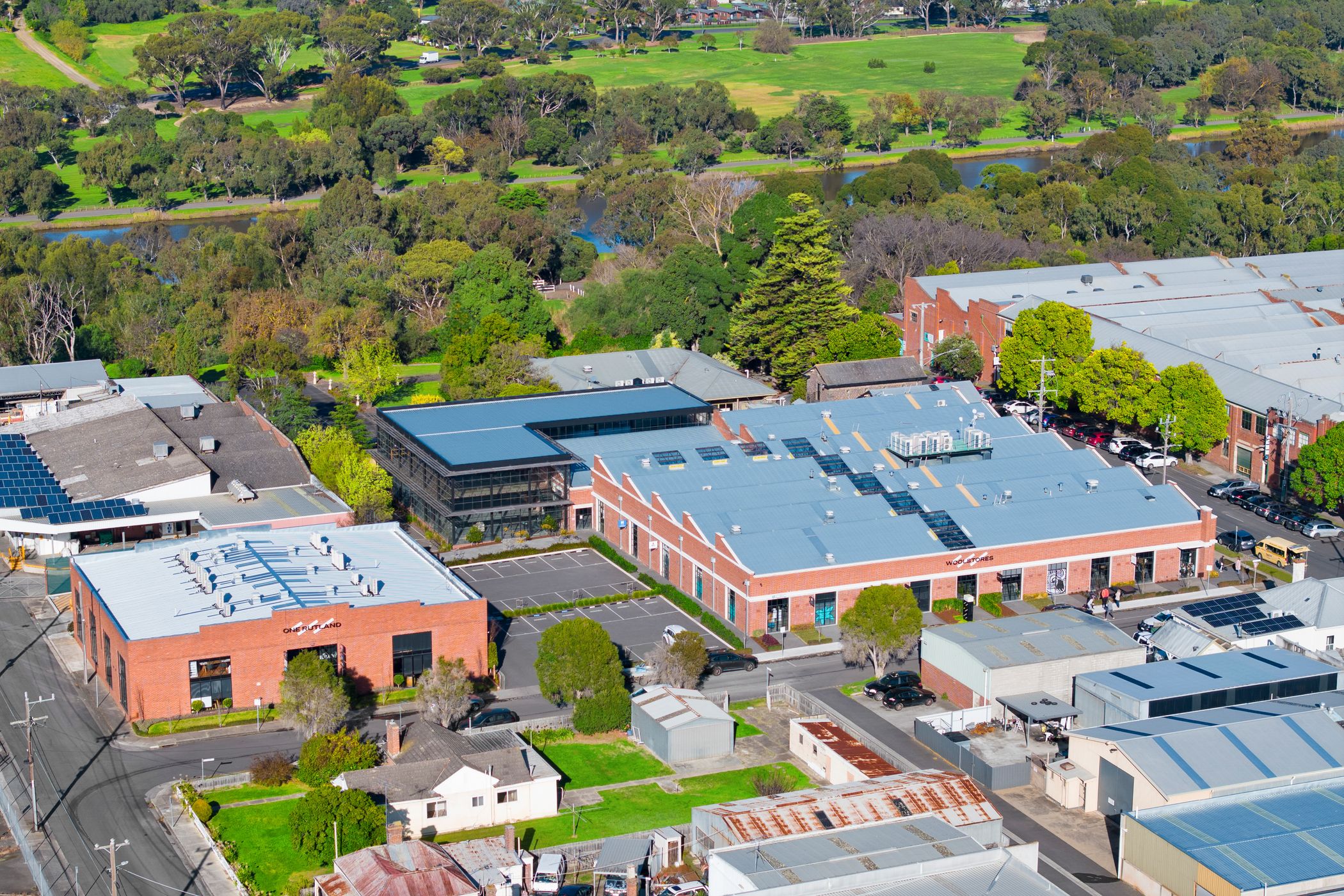 Aerial view of a large red brick complex, with a double story extension added to the back, car parks are at the front and in the background are lush green trees and mowed lawns, Woolstores owned by Hamilton group