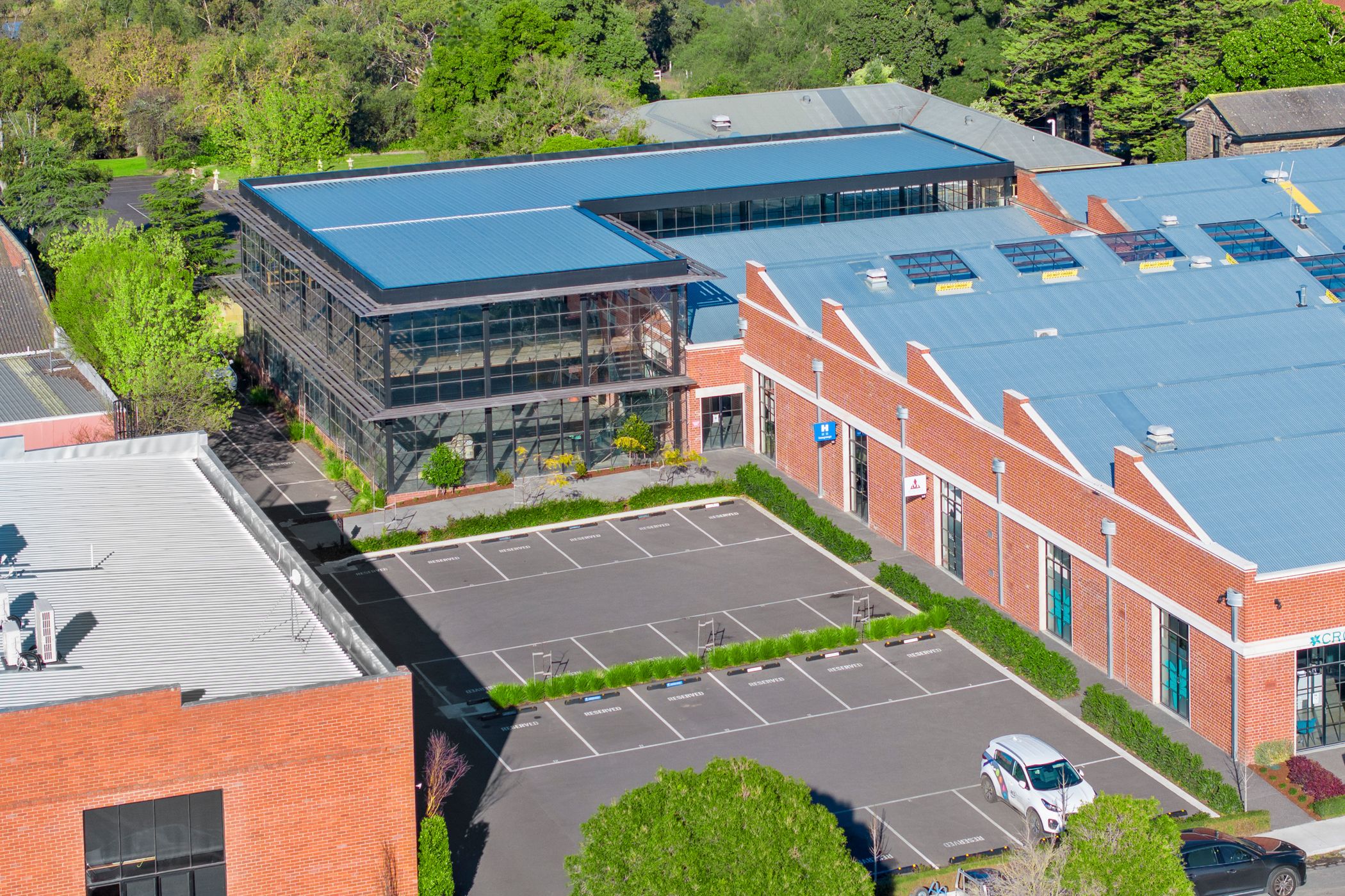Aerial view of a large red brick complex, with a double story extension added to the back, car parks are at the front and in the background are lush green trees and mowed lawns, Woolstores owned by Hamilton group