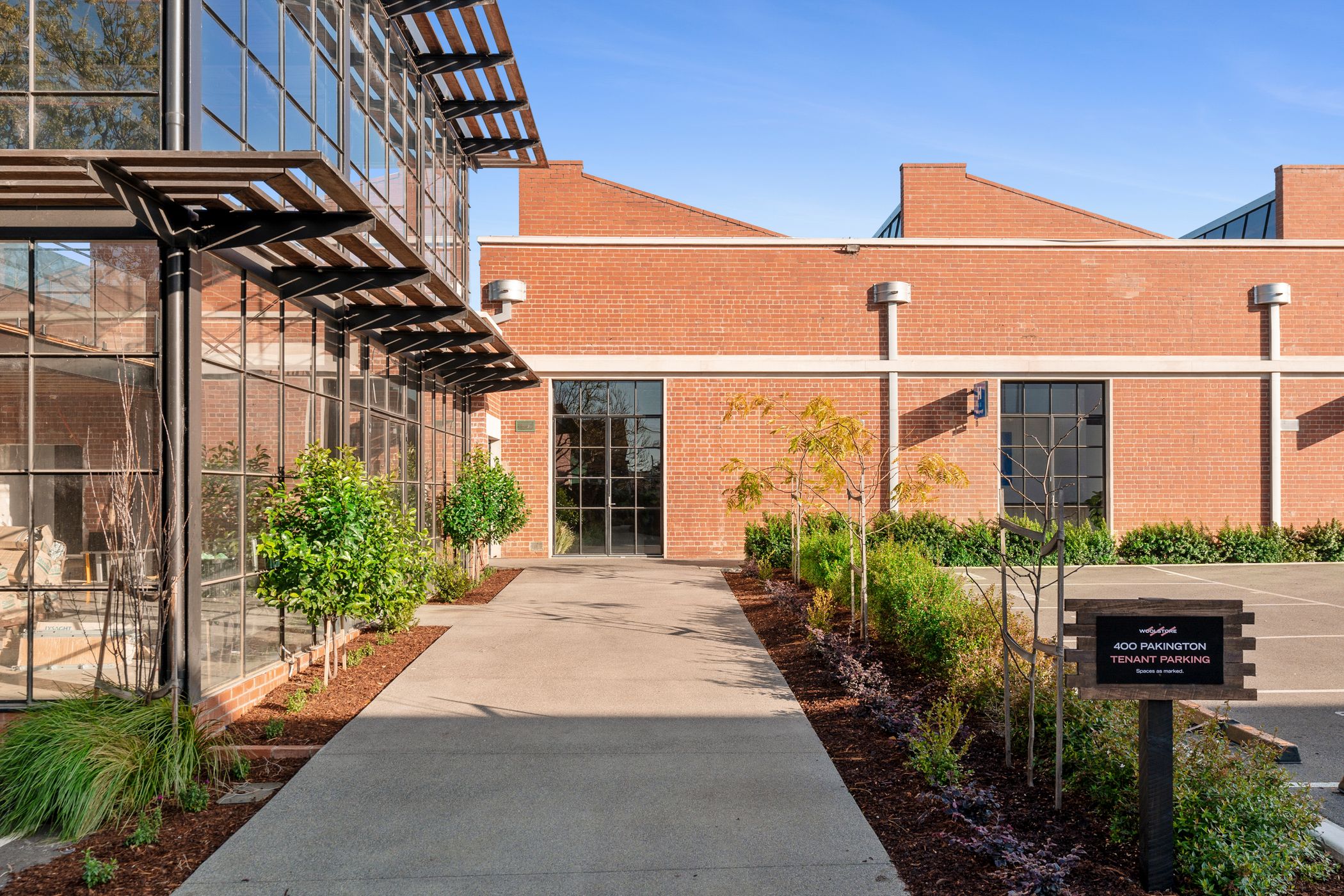 Long red brick facade with with sawtooth roof, black doors and windows are spread throughout, a large black building stands to the left with floor to ceiling T-Bar windows, heavy timber awning runs along both levels, Woolstores Geelong build by Hamilton Group