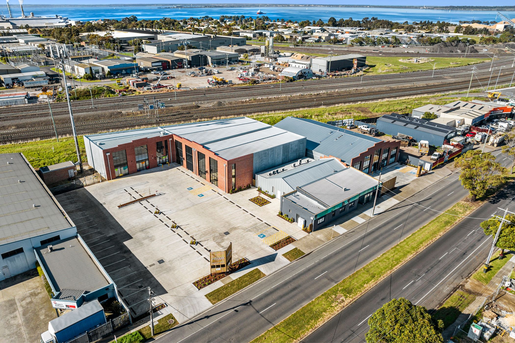 Aerial view of industrial factory area. two large brick sheds with T-bar windows fitted to the front, corrugated iron roof. Multiple train lines behind and ocean in the distance. Hamilton group Geelong