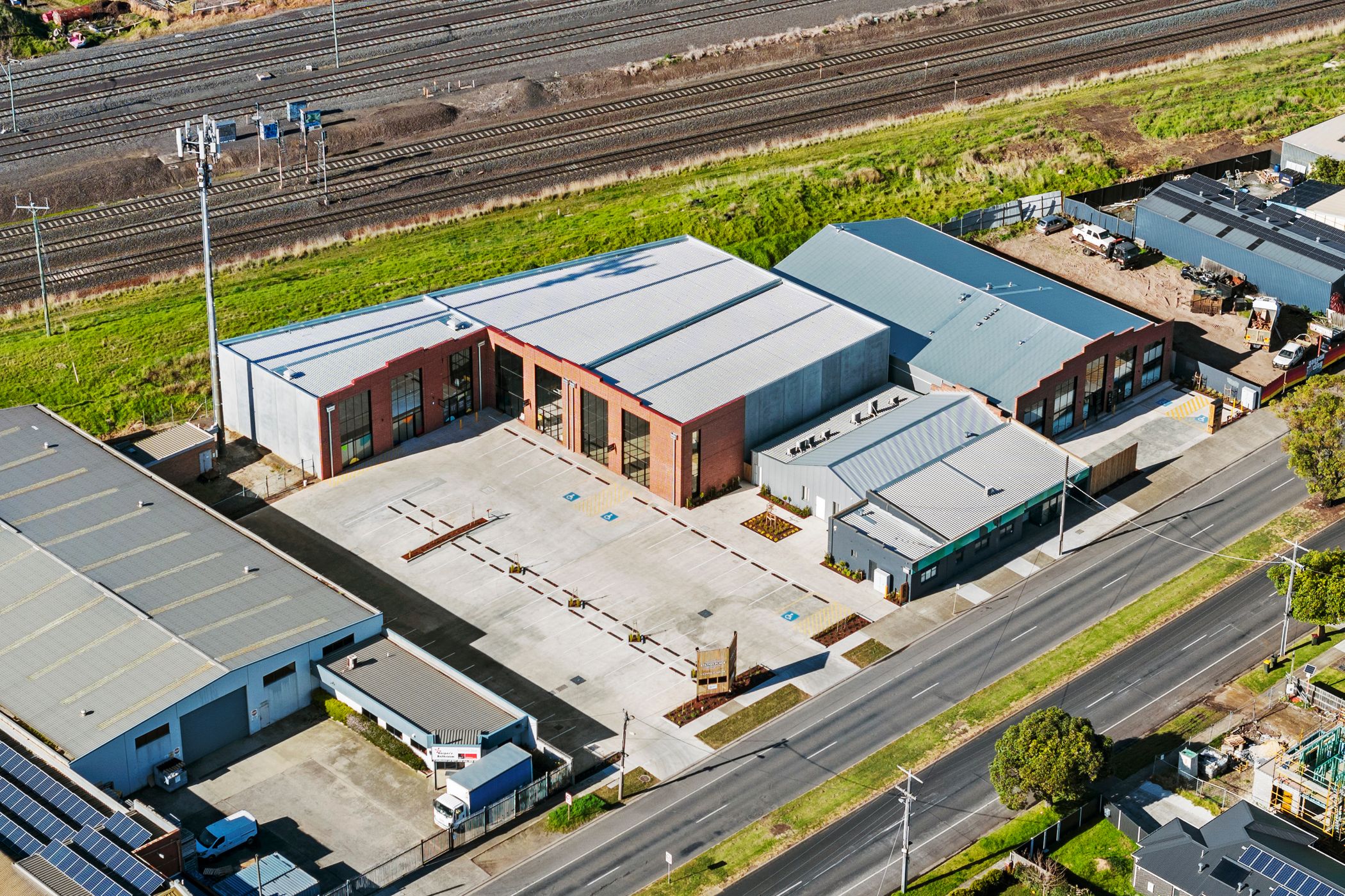 Aerial view of industrial factory area. two large brick sheds with T-bar windows fitted to the front, corrugated iron roof. Multiple train lines behind and ocean in the distance. Hamilton group Geelong