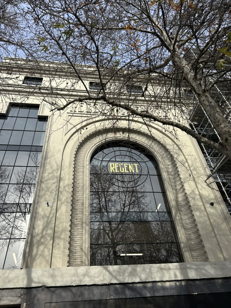 Facade of the historic Regent Theatre in Geelong, Victoria, featuring a grand arched window with 'Regent' signage, intricate architectural details, and leafless tree branches in the foreground.