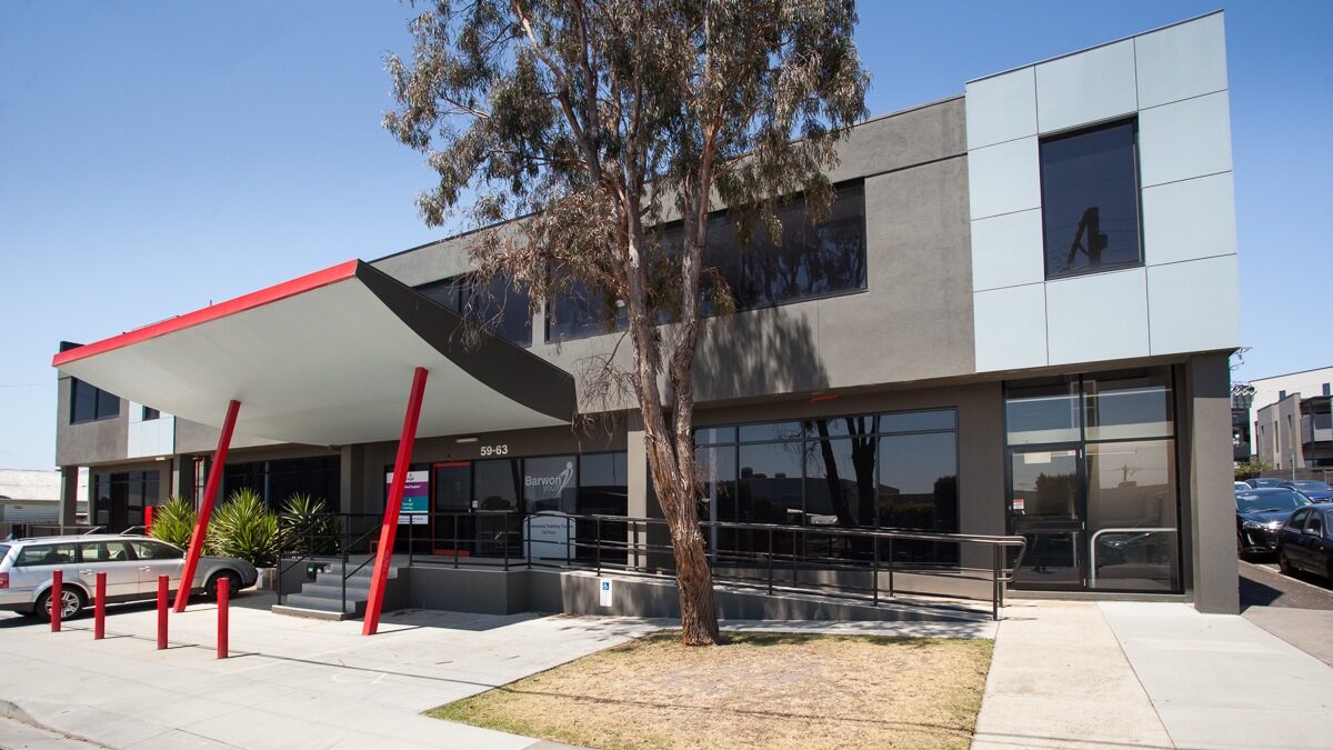 Clear blue skies above, dark grey building featuring architecturally designed awning stretching out, a yellow patch of grass is home to a tall lush tree, Leased by Hamilton Property Specialists