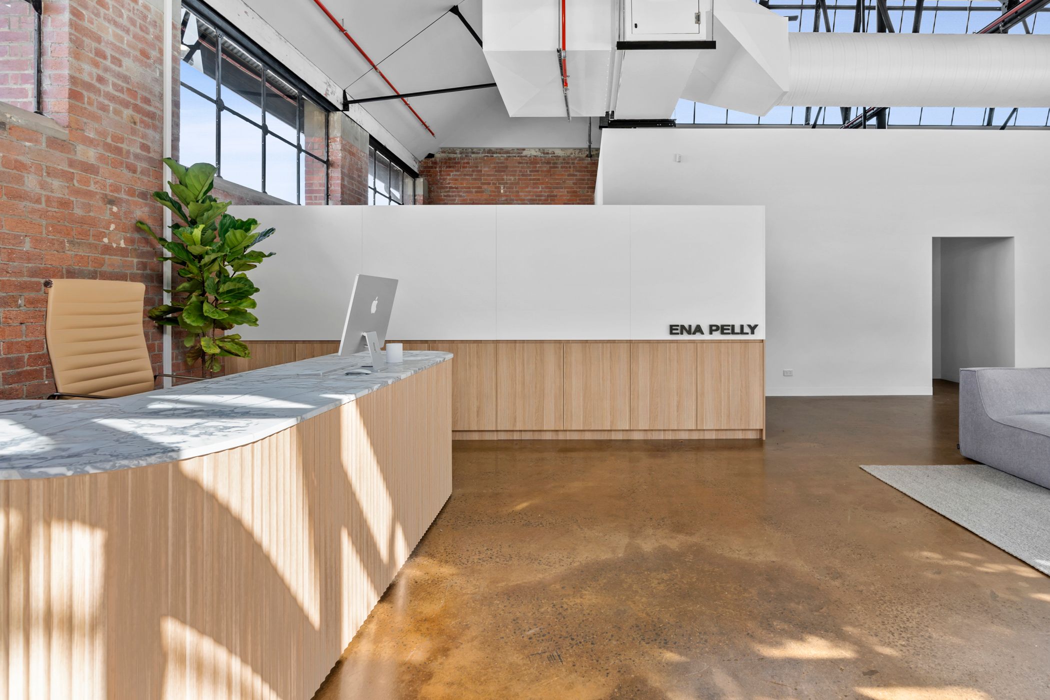 Minimalist reception area featuring a curved marble desk, warm wood accents, exposed brick walls, and industrial style windows. A modern, elegant workspace with natural lighting curated by Hamilton Spaces