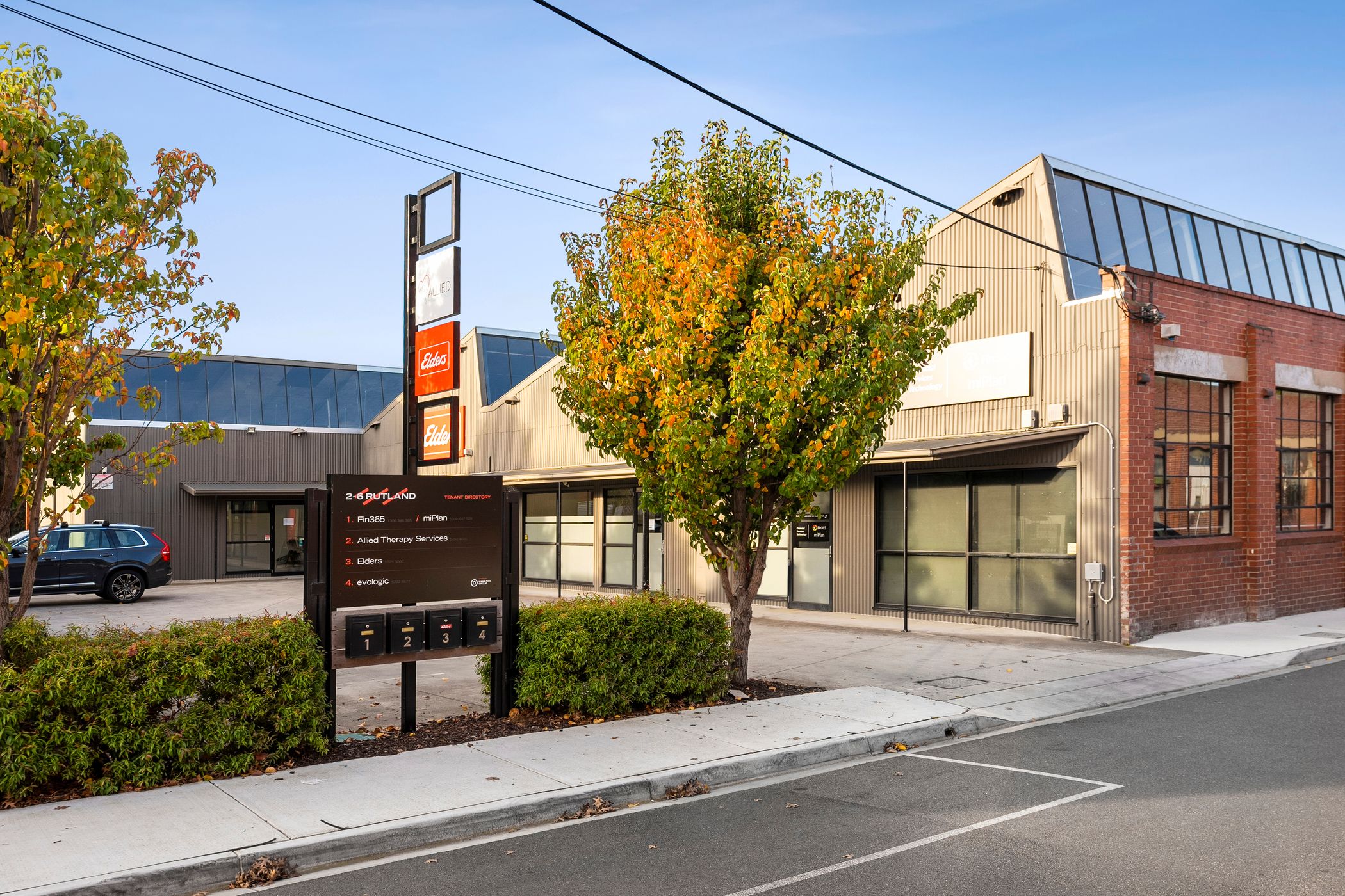 Old Black industrial warehouse turned into modern workspace, red brick and tbar wall lines one side, small carpark in the front featuring one car, a few trees around the carpark and a clear blue sky above, Hamilton Property Specialists
