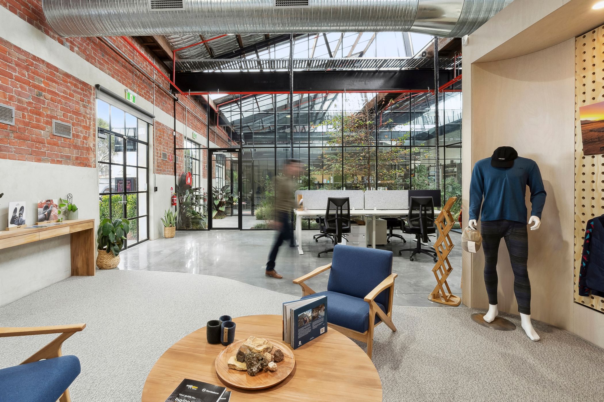 Internal view of a fun office space, this space has low blue sitting chairs surrounding a round timber table, the area has half carpeted part and half polished concrete floors, a T-bar window wall runs across the back, Woolstores precinct built by Hamilton Property specialists