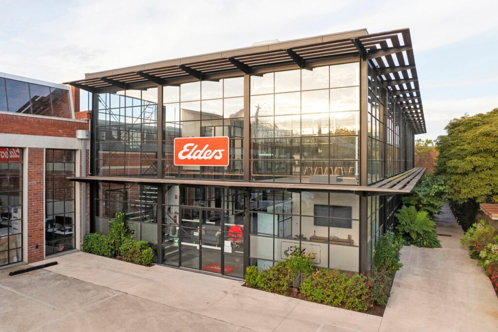 Tall building with Tbar window walls, two steel double doors and a timber awning running the length of the building, plant life surrounds the building - Hamilton group construction