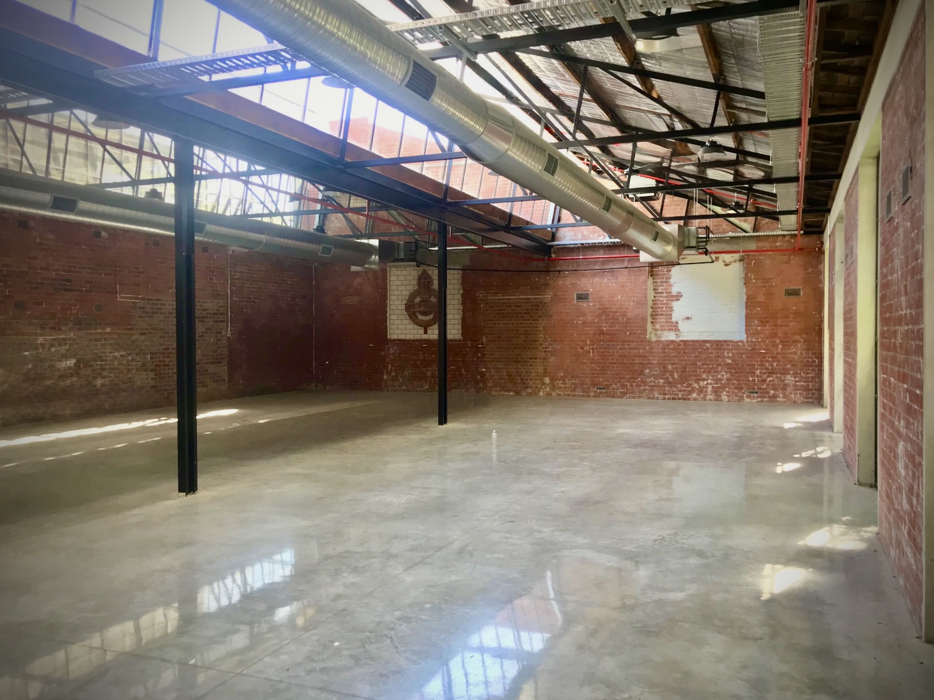 Freshly polished concrete floors, reflecting the out side sunlight, red brick walls filled with tbar windows and doors, exposed air conditioning duct above - Hamilton Spaces