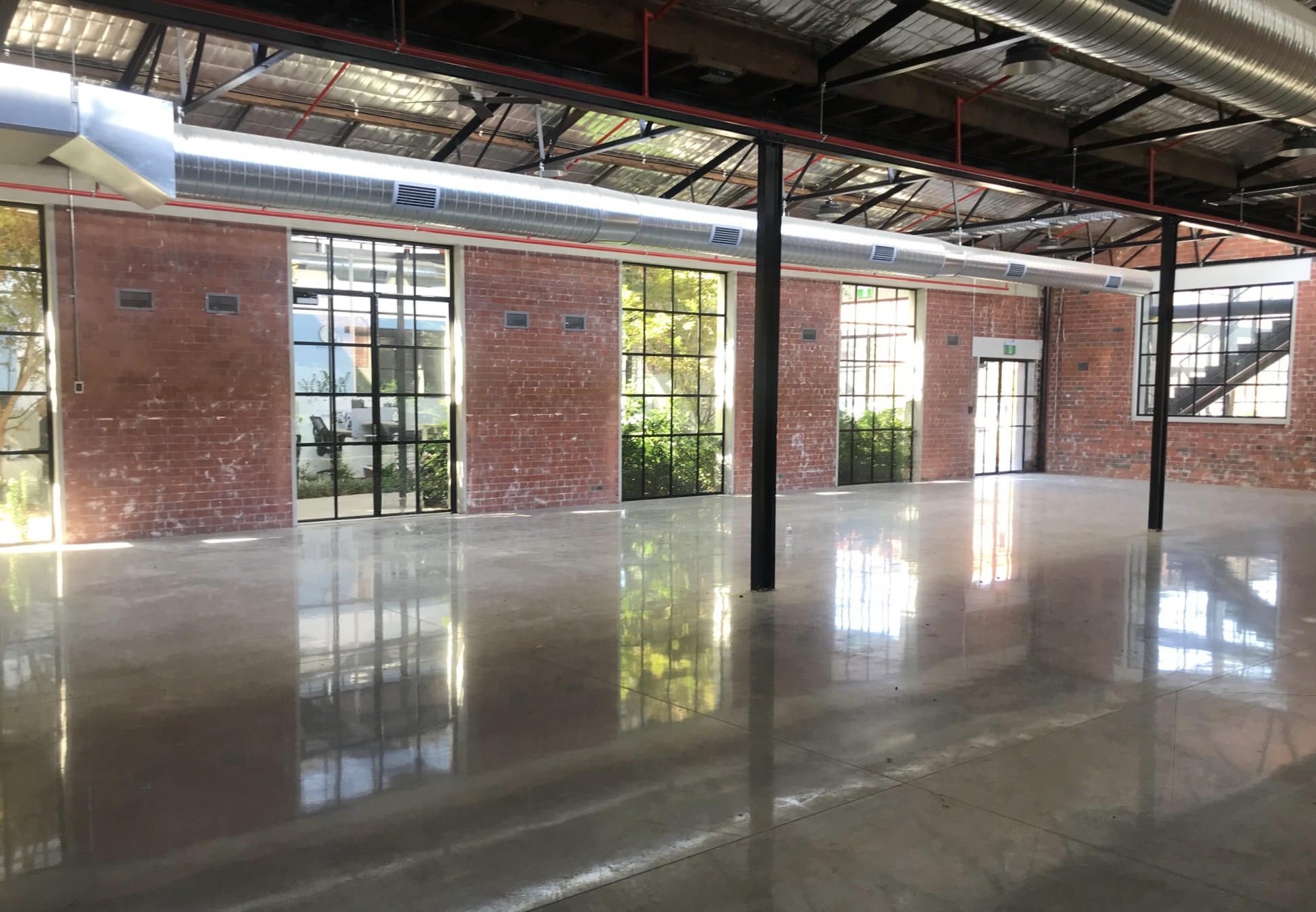 Freshly polished concrete floors, reflecting the out side sunlight, red brick walls filled with tbar windows and doors, exposed air conditioning duct above - Hamilton Spaces