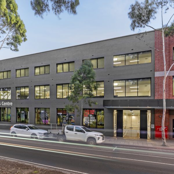 Wide view of large building, multiple windows across three levels, small awning above the front door, street runs in front of the building with two cars parked, sign on the front of the building says "NAB Business Centre", Owned by Hamilton Property Group Geelong