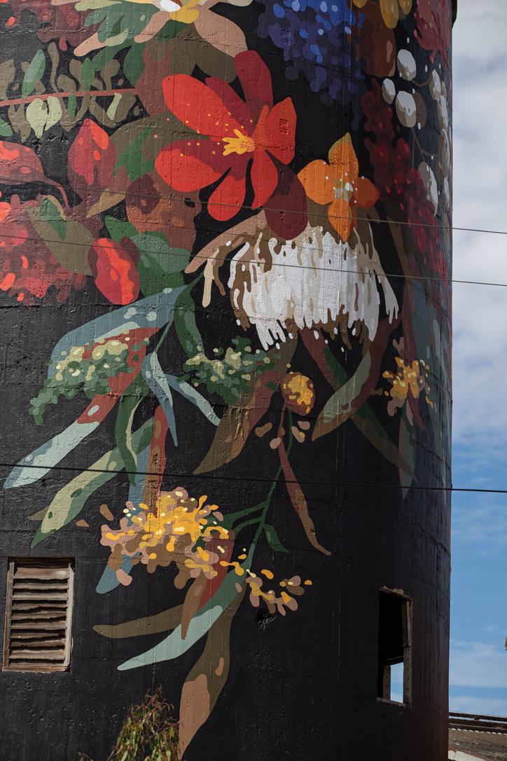 Detailed close-up of the water tower mural, showcasing vibrant flowers with textured brushstrokes and layered colours like red, yellow, green, and white set against a dark, dramatic backdrop. art by Sai Neoh at Federal mills