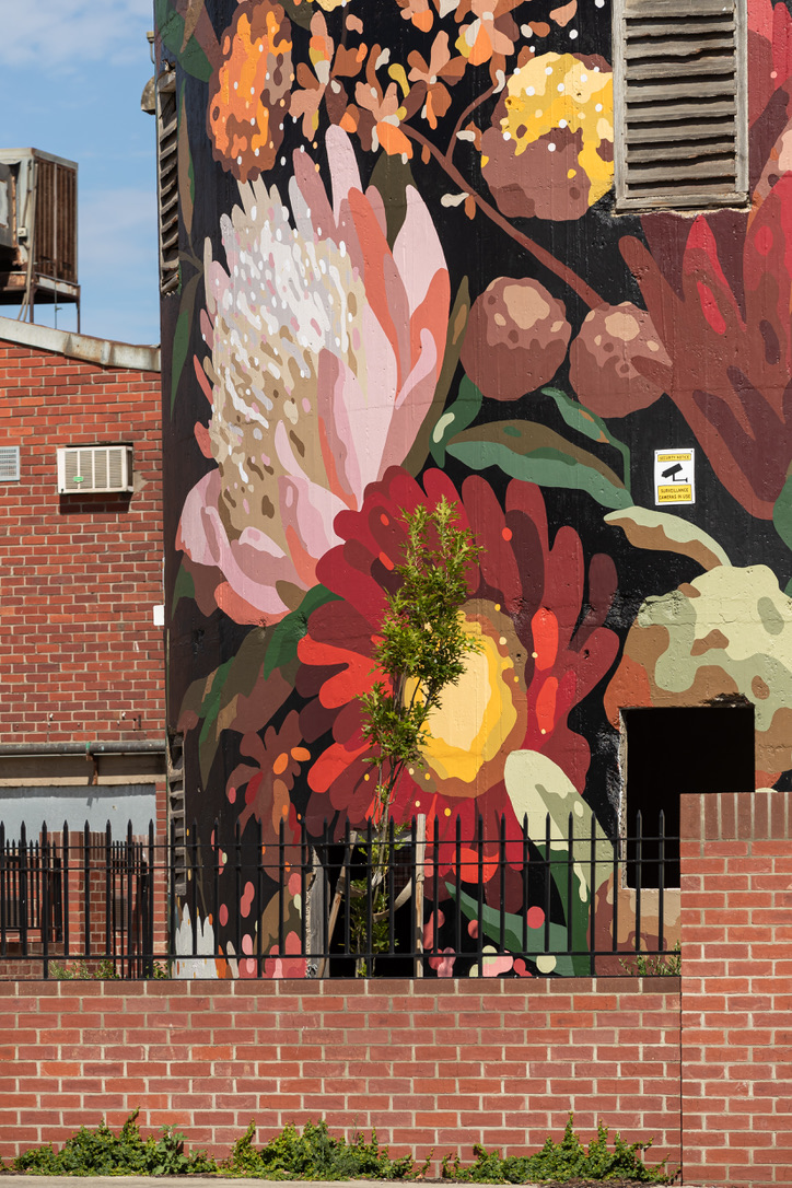 Close-up view of the water tower mural, highlighting intricate floral details with layered brushstrokes, rich textures, and vibrant colors including reds, yellows, greens, and whites against a dark background. Federal Mills, owned by Hamilton Group Geelong