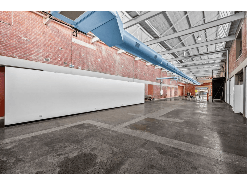 Long red brick warehouse, polished concrete floors, with steel beams running across the roof, a large air con vent is running the length of the building getting smaller the further it gets, a white petition wall is on the right, Hamilton Property Specialists