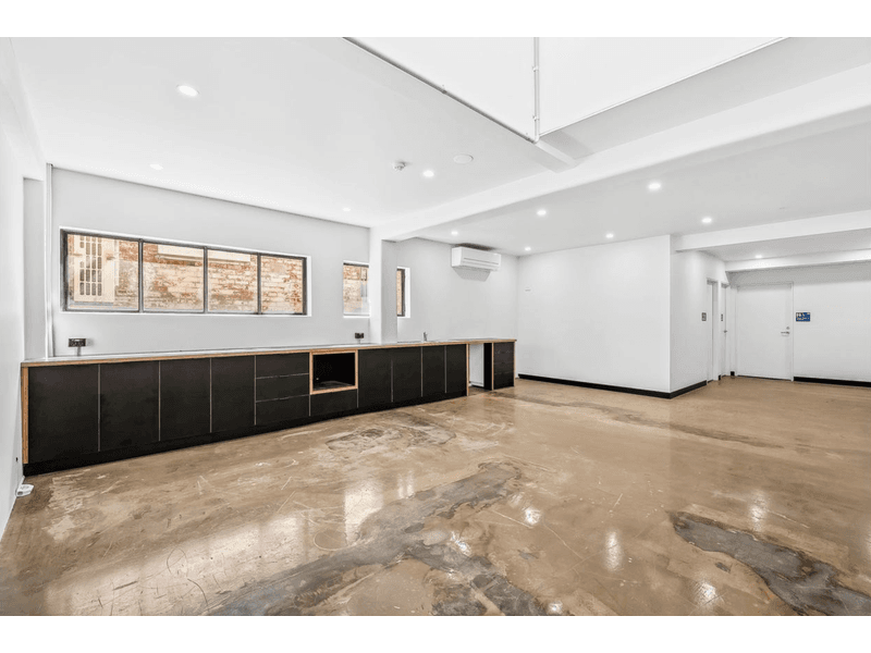 Open kitchen space, with polished concrete floors, white walls surround the room, windows are on the far wall with a set of black cupboards below them, out side the window is a red brick wall with a aircon vent attached to the wall, Hamilton Group Geelong