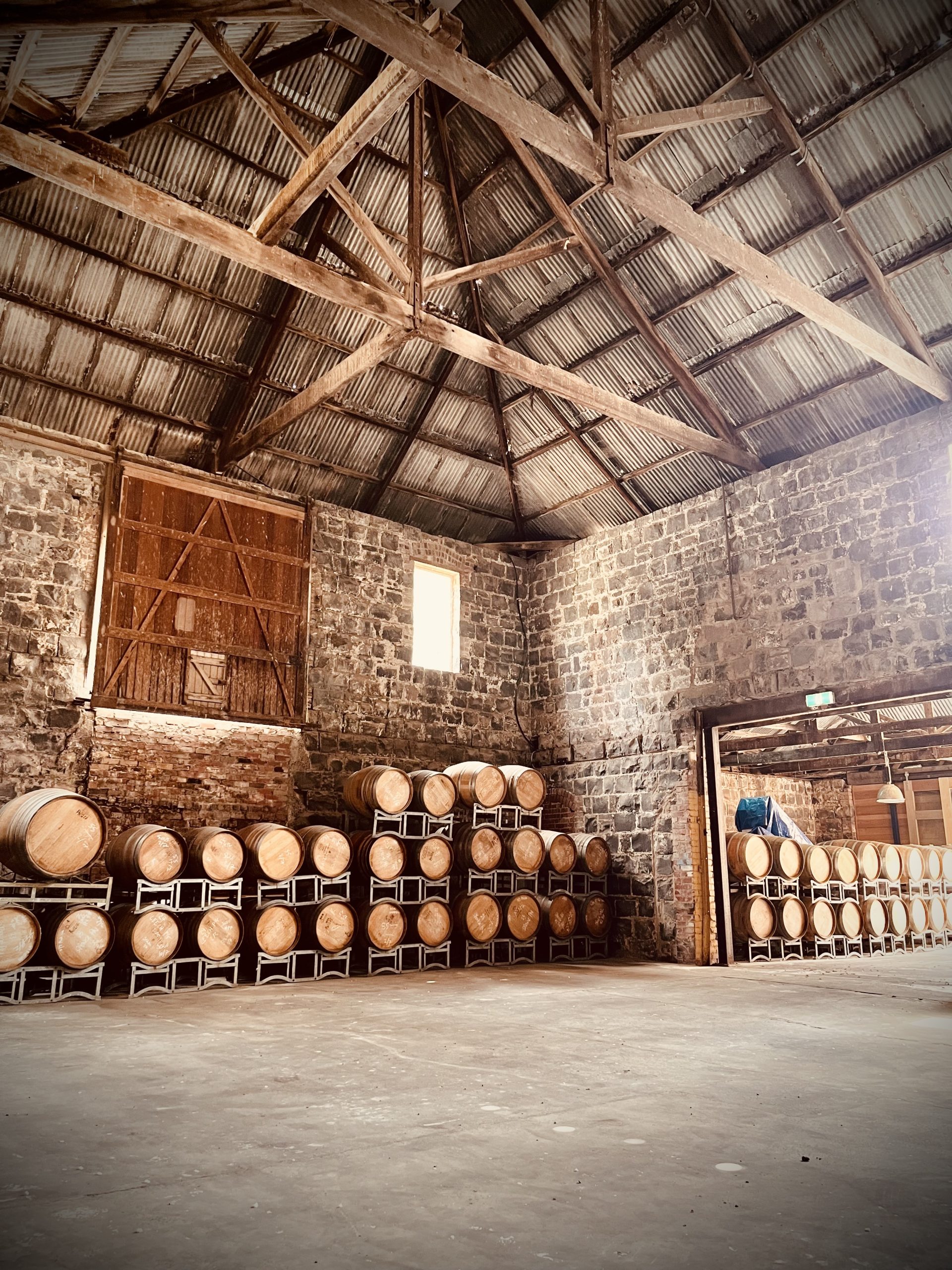 Timber drum holding area within a blue stone warehouse, old timber trusses holding up a rusted corrugated iron roof, a large timber hardwood sliding door is elevated off the ground on the back wall, this building is being renovated by Hamilton property group Geelong