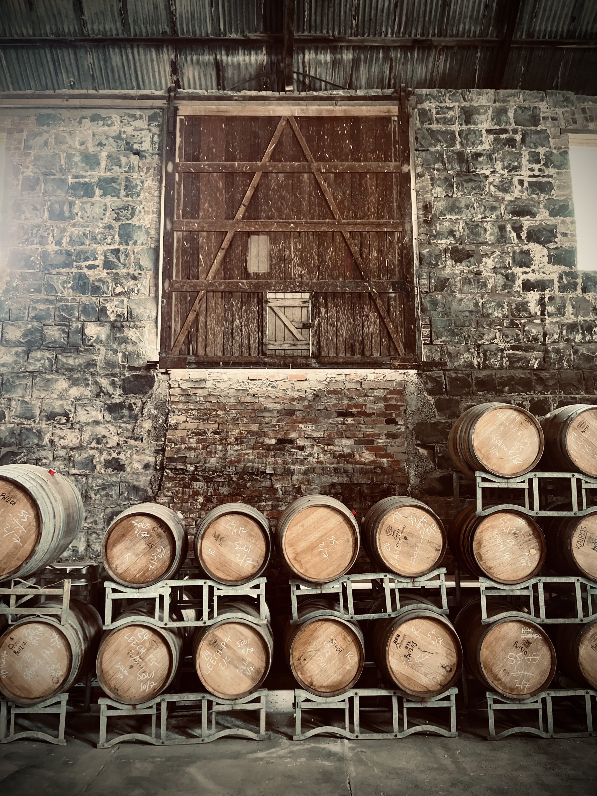Timber drum holding area within a blue stone warehouse, old timber trusses holding up a rusted corrugated iron roof, a large timber hardwood sliding door is elevated off the ground on the back wall, this building is being renovated by Hamilton property group Geelong