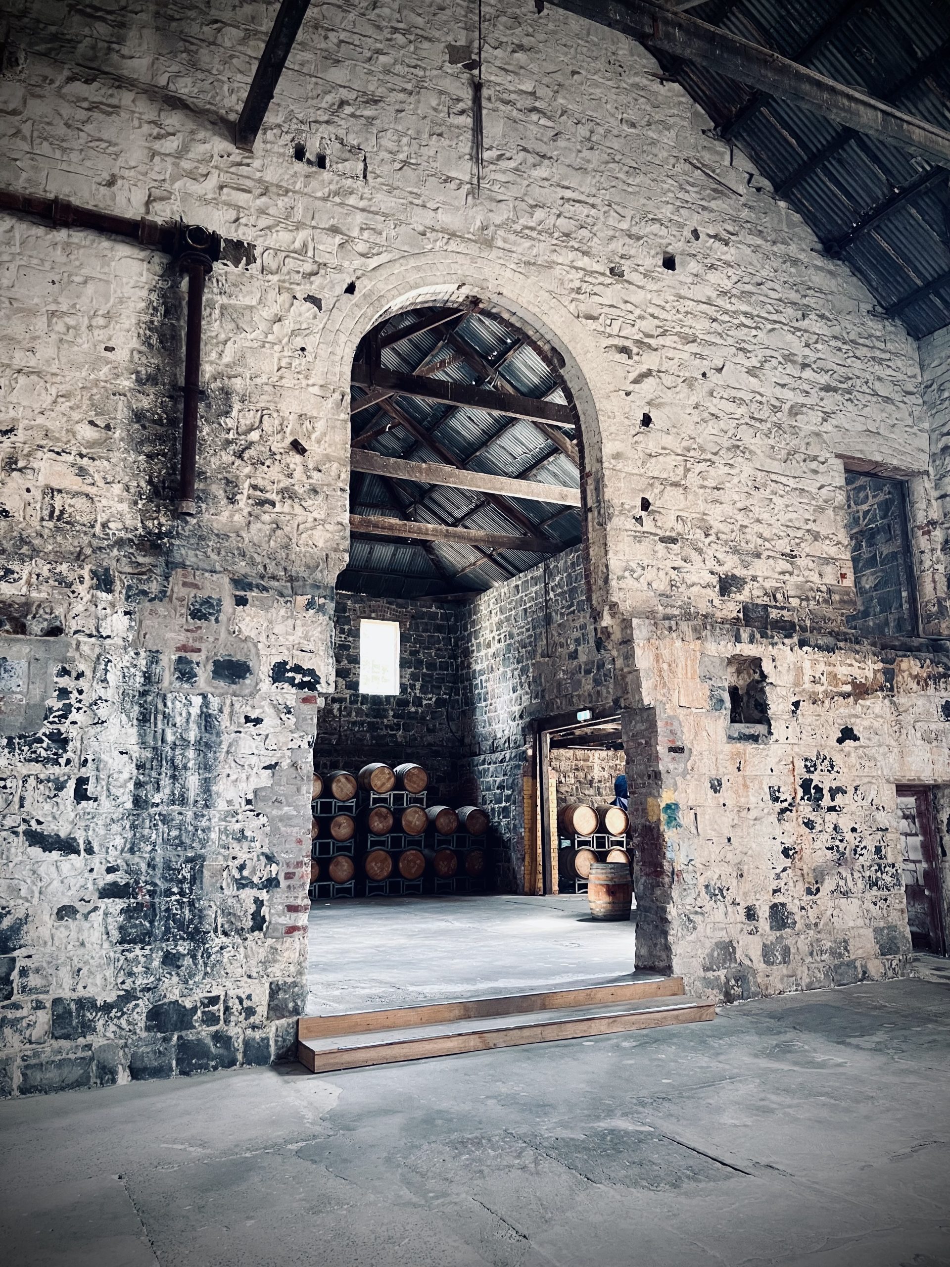 Very old blue stone wall featuring a large archway leading into a timber barrel storage area, timber trusses fill the roof holding up the old corrugated iron roof, this old paper mill mill is being renovated by the skilled team at Hamilton Property Group, Geelong